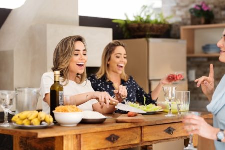 Foto mostra mulheres gêmeas idênticas dividindo uma refeição em uma mesa. Alimentação saúdavel, comer frutas e verduras