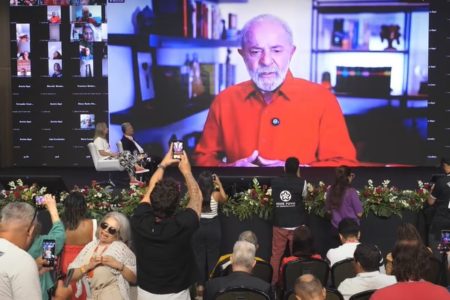 Foto colorida de auditorio com o pesidente Lula em telão - Metrópoles