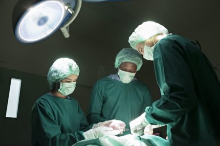 Imagem colorida de três médicos em sala de cirurgia - Metrópoles