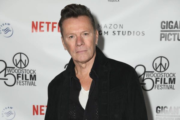 Imagem colorida de Larry Mullen Jr. usando roupa preta em tapete vermelho - Metrópoles