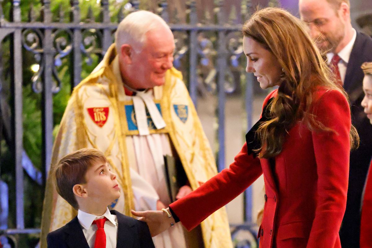 Foto colorida de mulher e menino conversando. Atrás dele tem um homem com roupa religiosa - Metrópoles