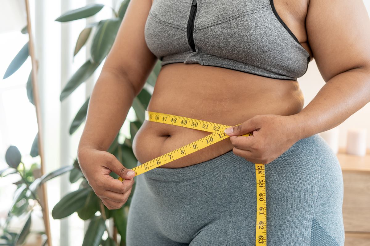 Foto colorida de mulher com fita métrica na barriga. Ela usa roupas de treino - Metrópoles
