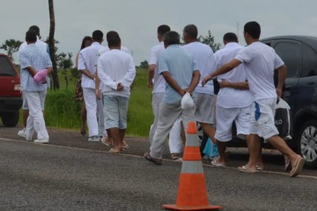 Imagem colorida de detentos de branco algemados de costas