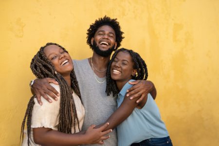 três irmãos negros abraçados sorrindo para a câmera. Metrópoles