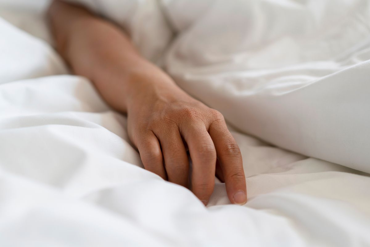 Foto colorida de uma mão na cama - Metrópoles