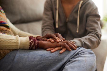 Imagem colorida de criança negra apoiando as mãos em colo de mulher também negra. - Metrópoles