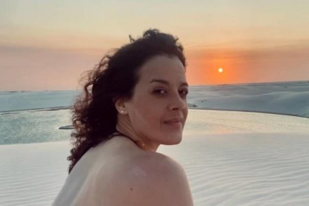 foto colorida de mulher branca de cabelos cacheados com praia ao fundo - metrópoles