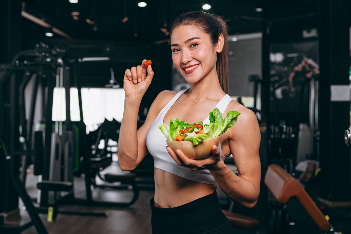Foto colorida de mulher segurando bowl de salada em uma academia - Metrópoles