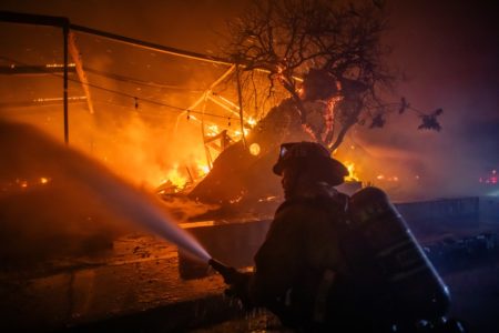 Imagem colorida de bombeiro tentando controlar as chamas na em casa - Metrópoles