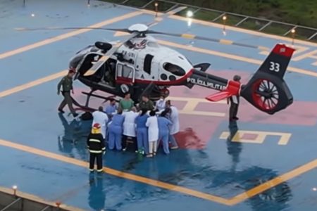 Imagem colorida de mulher saindo de maca de helicóptero águia. Metrópoles