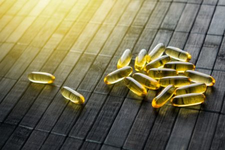 Pílulas e capsulas de protetor solar dourado em fundo preto de madeira à luz solar. Os suplementos dietéticos protegem a pele do sol. Metrópoles