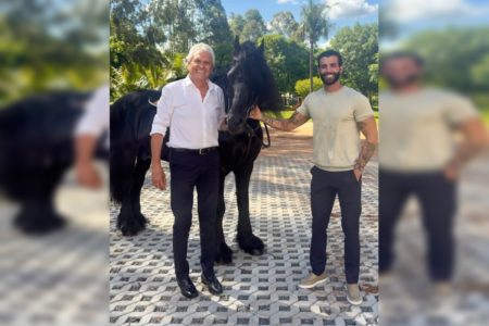 Imagem colorida de Caiado e Gusttavo Lima com um cavalo preto em mansão
