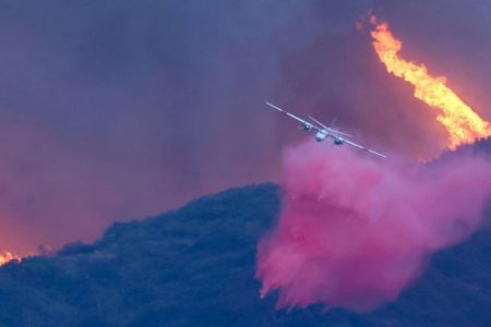 Foto colorida de avião derrubando mistura rosa sobre árvores que pegavam fogo - Metrópoles
