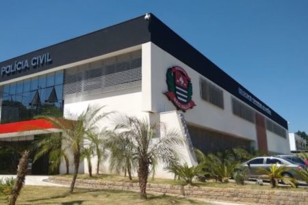 Imagem colorida do 1° DP de Jundiaí, pintado em branco, preto e vermelho. Também são visíveis árvores pequenas e um carro preto estacionado. - Metrópoles