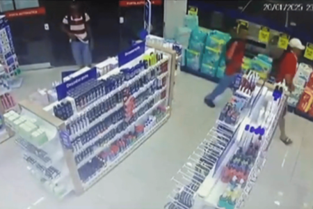 Imagem colorida de uma câmera de vigilância de uma farmácia. As imagens mostram três homens jovens entrando no estabelecimento, um está com a mão na cintura - Metrópoles
