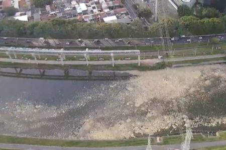 Imagem colorida mostra trecho de rio visto de cima. No meio da água do rio há uma mancha de cor clara, aparentando espuma - Metrópoles