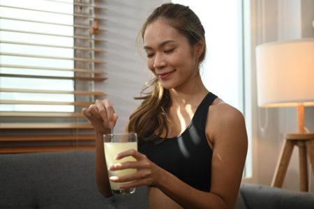 Foto colorida de mulher misturando algo dentro de um copo de suco - Metrópoles