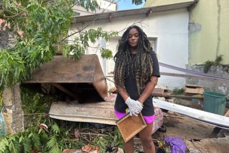 Imagem colorida de jovem em frente a casa destruída