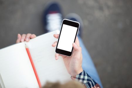 Imagem colorida de pessoa usando celular enquanto segura um caderno