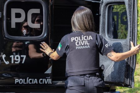 Foto colorida de uma agente da Polícia Civil fechando a porta da viatura - Metrópoles