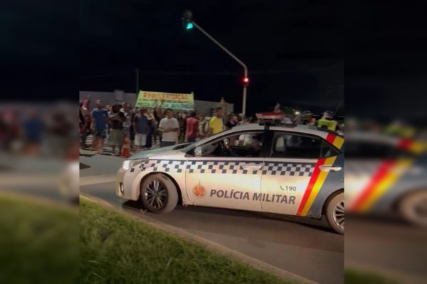 Imagem de moradores protestando em uma rodovia. À frente, há uma viatura da PMDF