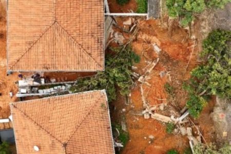 Imagens coloridas mostram visão aérea, feita por drone, de duas casas atingidas por lama após o deslizamento de terra