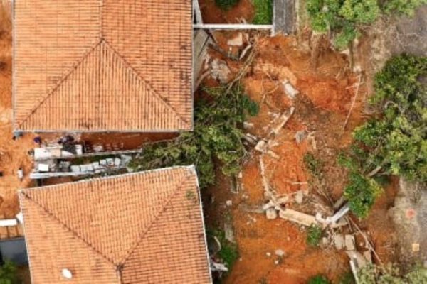 Imagens coloridas mostram visão aérea, feita por drone, de duas casas atingidas por lama após o deslizamento de terra