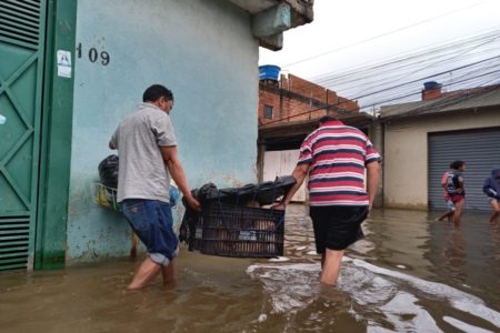 Imagem colorida de moradores ajudando vítimas de enchente. Metrópoles