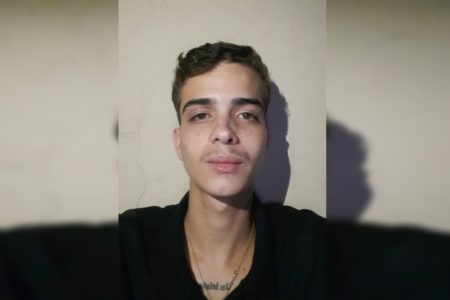 Imagem colorida de um jovem branco, de camiseta preta, cabelos pretos curtos