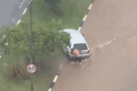 Imagem colorida de homem tentando tirar carro de avenida alagada em Guarulhos. Metrópoles