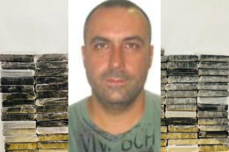 Retrato de homem branco, com barba por fazer, cabelo raspado com entrada, atrás do qual há tijolos embrulhados com saco plástico preto, empilhados em frente a parede branca - Metrópoles