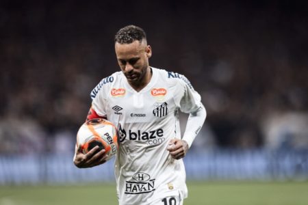 Imagem de Neymar, com a camisa do Santos, segurando uma bola com a mão direita e olhando para baixo - Metrópoles