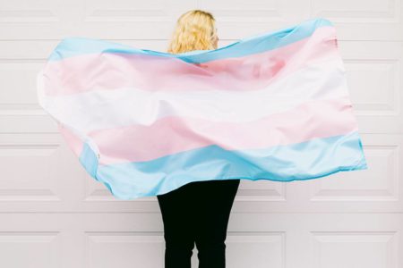 Mulher de costas segura bandeira trans - Metrópoles
