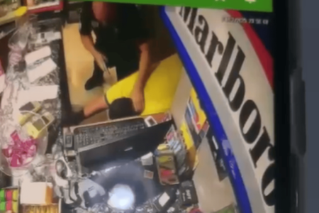 Imagem colorida de uma câmera de segurança da loja de conveniência que mostra o policial agredindo um homem de camiseta amarela com coronhadas - Metrópoles