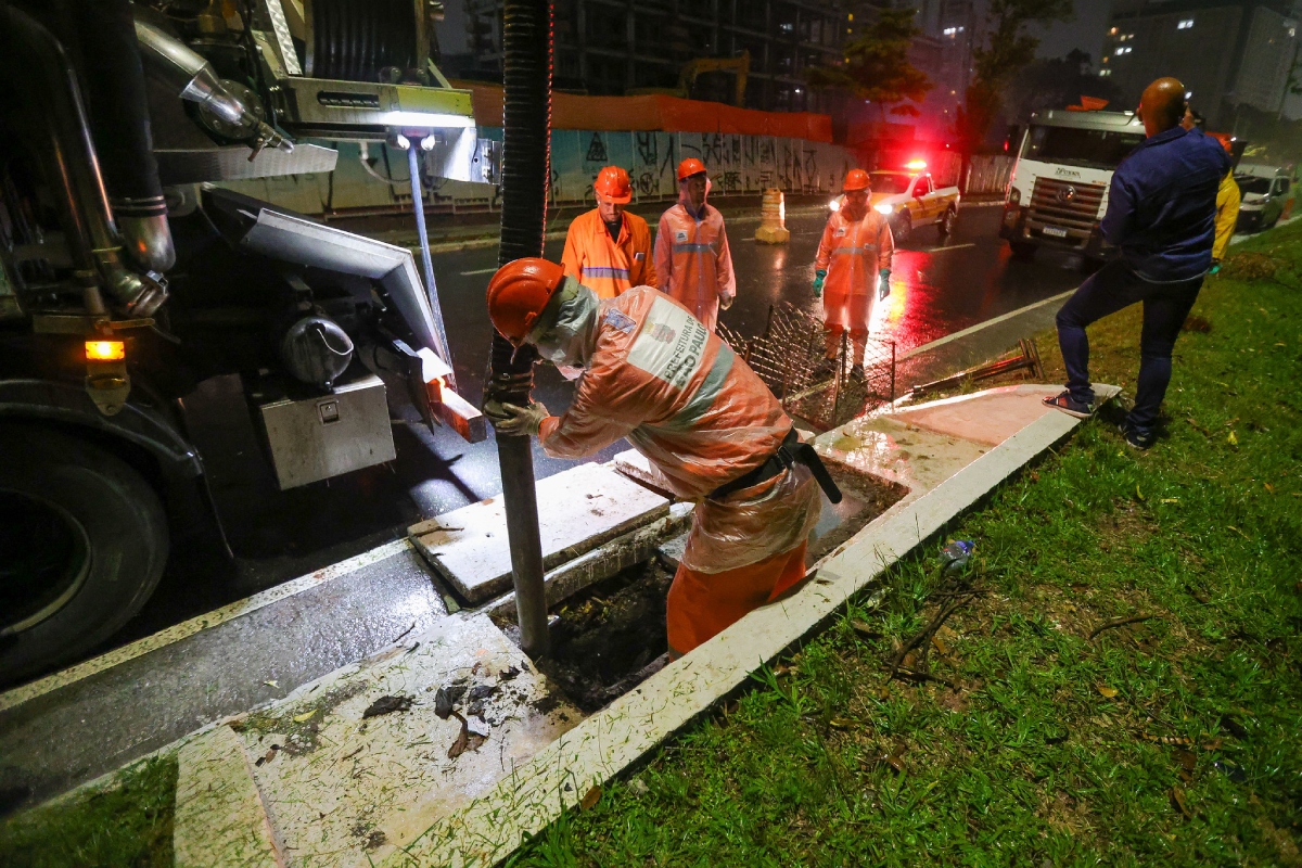 Foto colorida de homens trabalhando na limpeza de um bueiro - Metrópoles