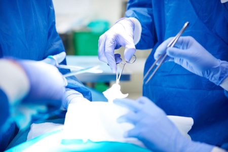 Foto colorida de mãos de médicos com luvas e equipamentos cirúrgicos - Metrópoles