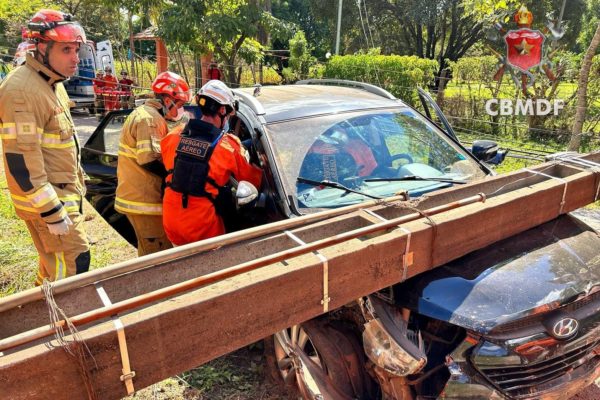Foto colorida de carro batido em poste com equipes do corpo de bombeiros
