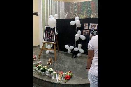 Imagem colorida de um memorial com balões brancos, fotos de vítimas e flores espalhadas - Metrópoles