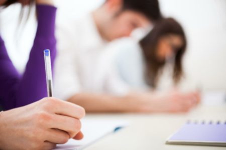 Estudantes com caneta na mão fazendo prova