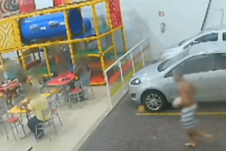 Imagem colorida de uma câmera de segurança mostra um homem sem camisa com um bloco de pedra na mão correndo em direção a outro homem sentado em uma lanchonete - Metrópoles