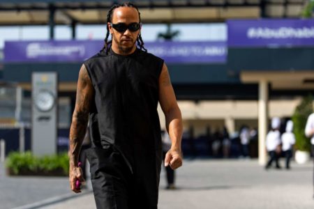 A imagem mostra o piloto Lewis Hamilton vestindo roupas pretas