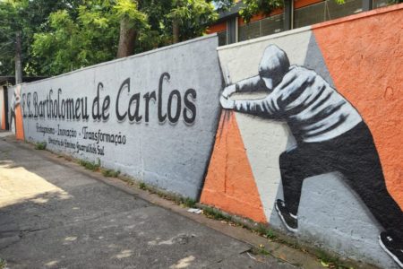 imagem colorida mostra fachada de escola. na parede está escrito o nome escola bartholomeu de carlos e há dois desenhos de pessoas