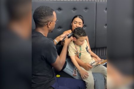 imagem colorida mostra um barbeiro, homem negro cortando cabelo de criança em colo da mãe - metrópoles
