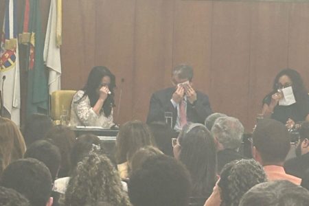Imagens coloridas mostram governador de SP, Tarcísio de Freitas, de terno escuro, sentado ao centro, enxugando lágrimas com lenço branco. Do lado esquerdo da imagem, a primeira-dama, Cristiane, também enxugando lágrimas