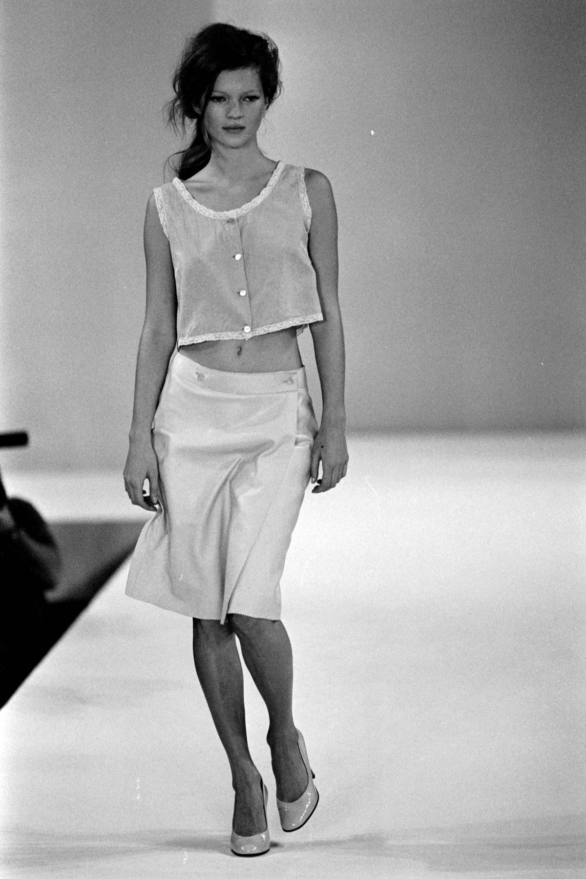 A imagem mostra a modelo Kate Moss desfilando em 1995