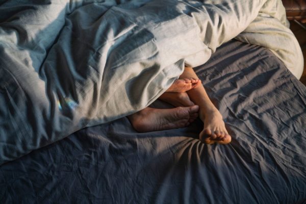 imagem colorida de dois pés em uma cama com lençois azuis