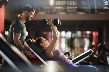 Mulher faz exercício de musculação com ajuda de personal - Metrópoles