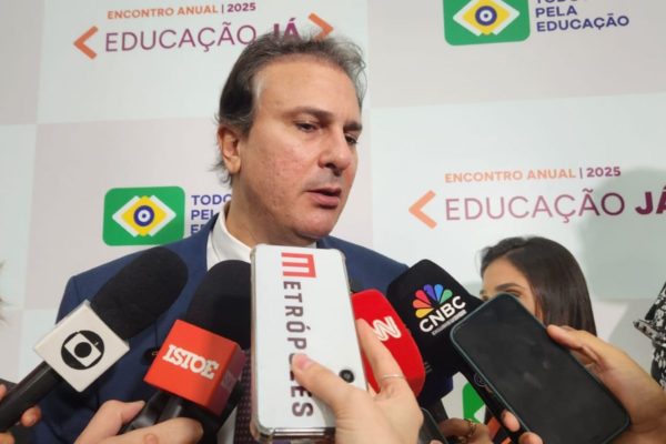 Imagem colorida do ministro da Educação Camilo Santana, homem branco de barba feita. Ele tem o olhar para baixo enquanto seis microfones e celulares estão apontados em direção a sua boca - Metrópoles