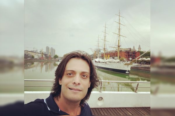Imagem de um homem branco, cabelos médios, camiseta azul