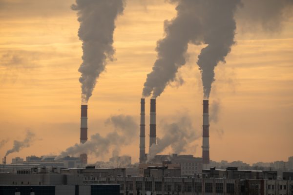 Usina elétrica a carvão com chaminés fumegantes contra o céu dramático do pôr do sol. Uso prejudicial de combustível em cidade grande. Metrópoles